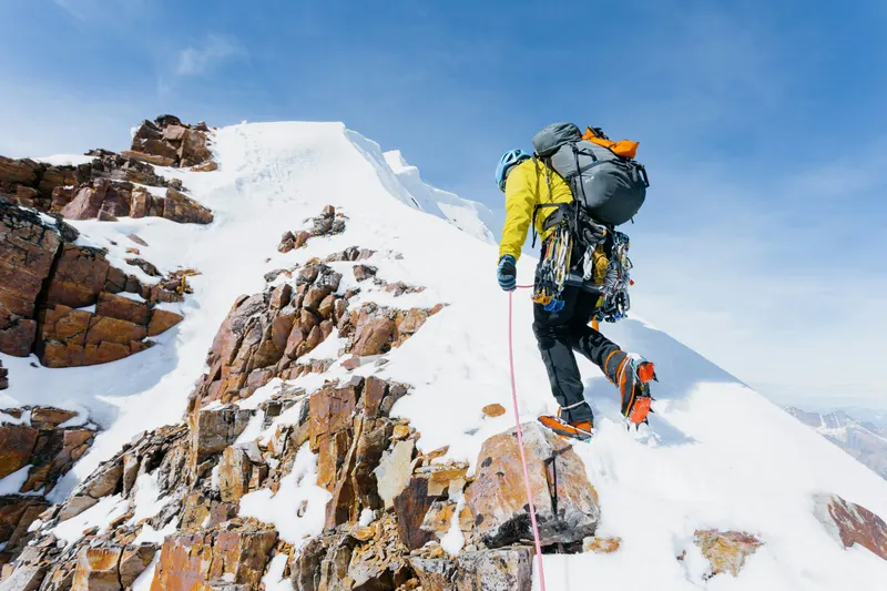 A climber roped up, cramponing along a rocky summit ridge