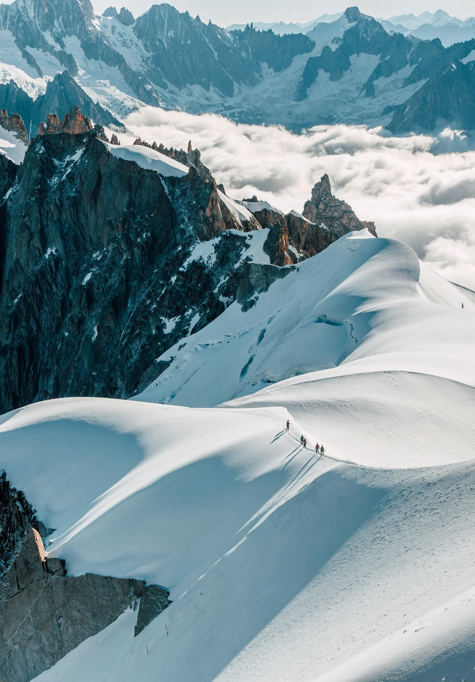 A rope team crossing a snow ridge above the clouds