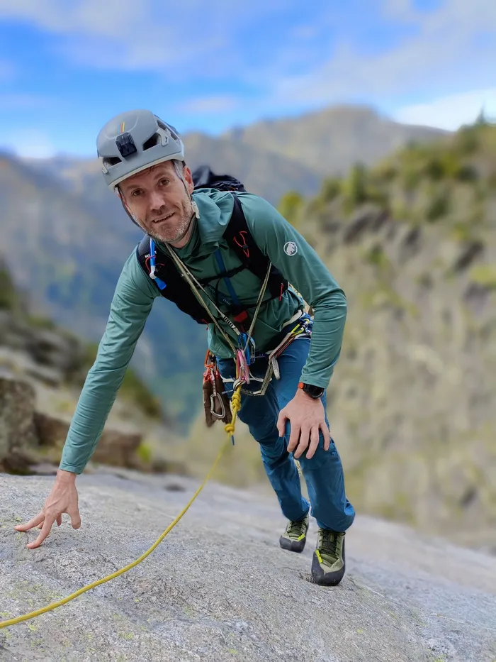 Olivier climbing on a granite slab, roped up in the mountains